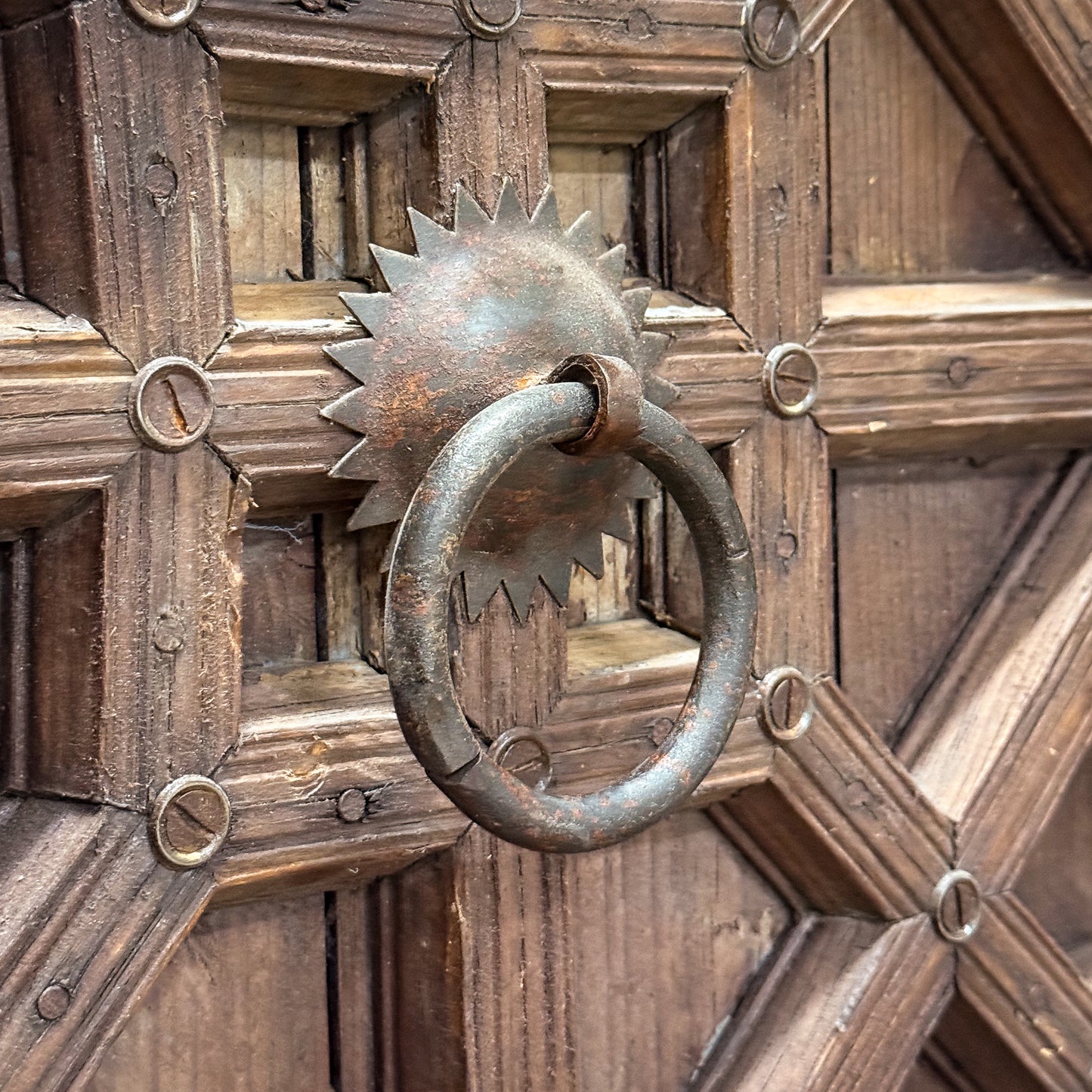 Rustic metal knocker on a wooden door with geometric patterns