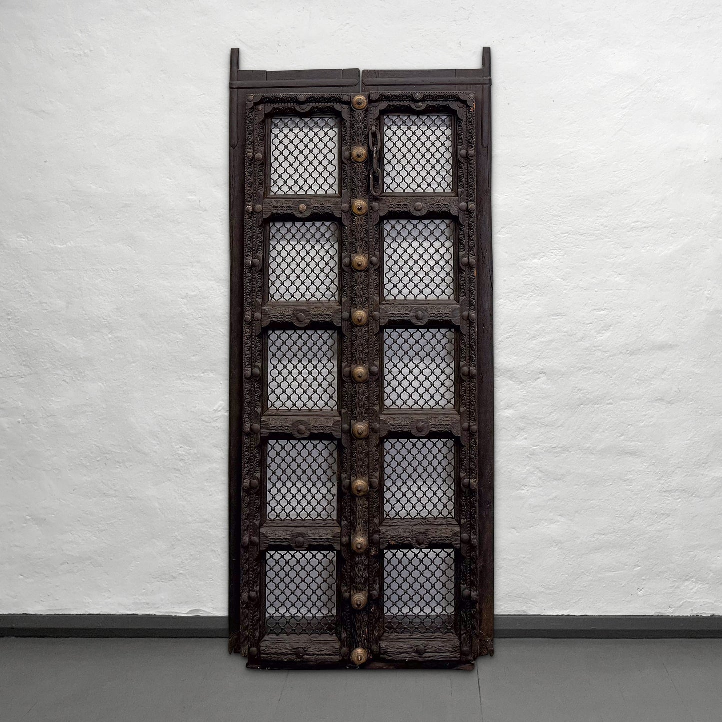 Decorative wooden door with mesh design and brass fixtures against a white wall.