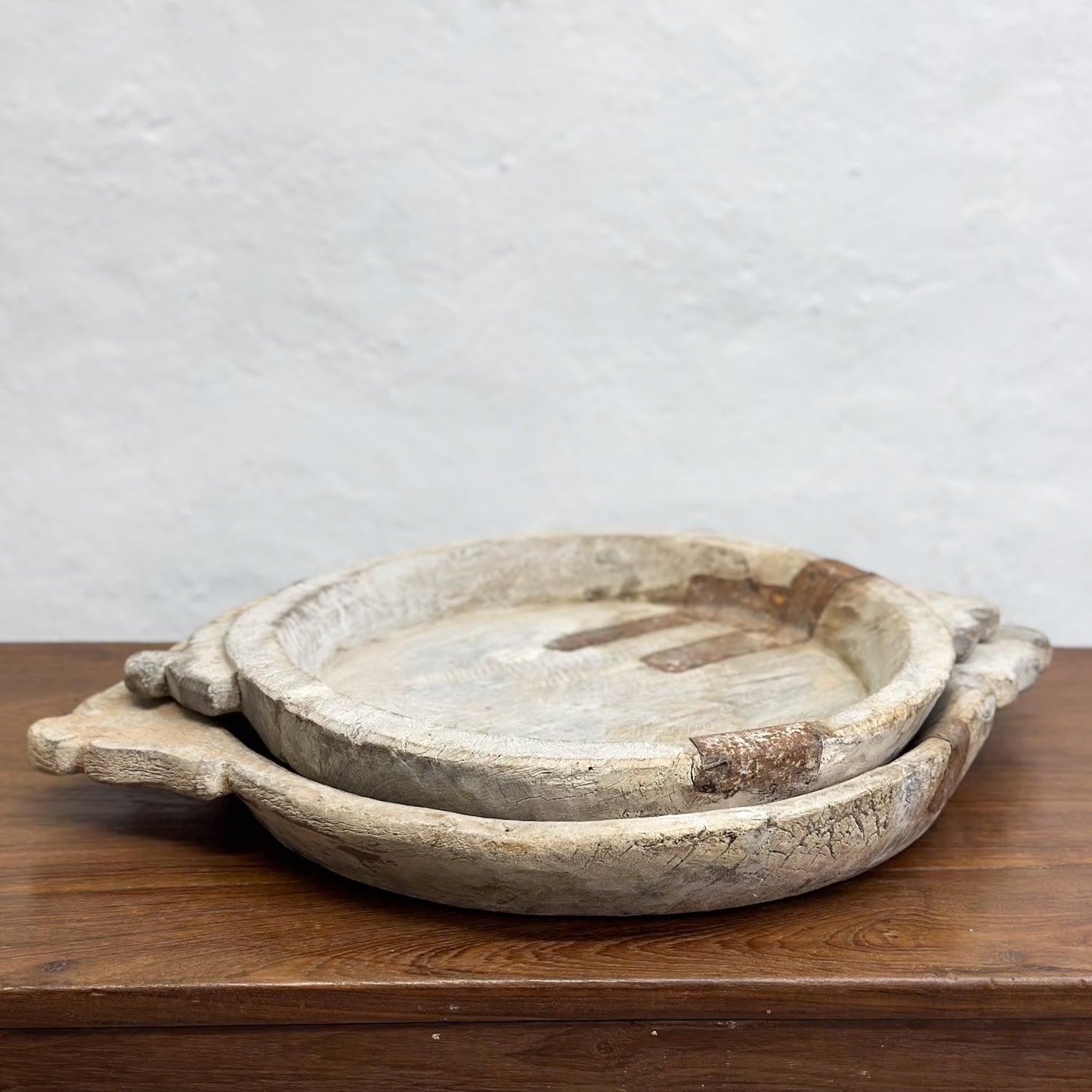 A beige decorative bowl with iron detail, placed on a wooden surface against a plain wall.