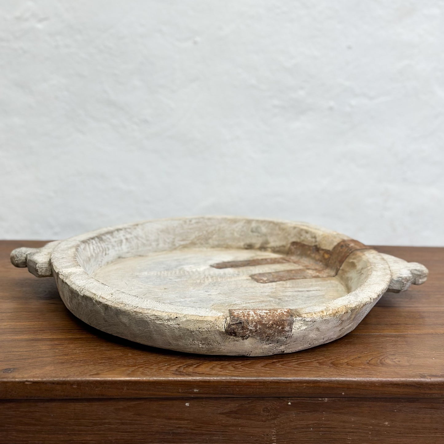 A beige decorative bowl with iron detail, placed on a wooden surface against a plain wall.