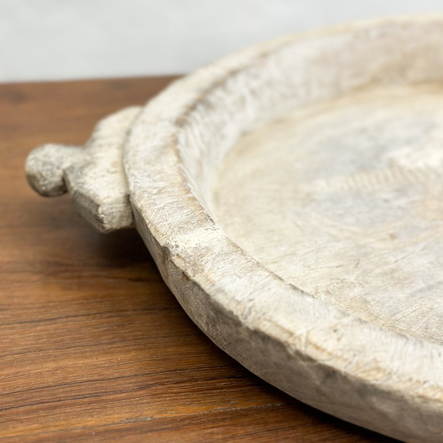 A beige decorative bowl with iron detail, placed on a wooden surface against a plain wall.