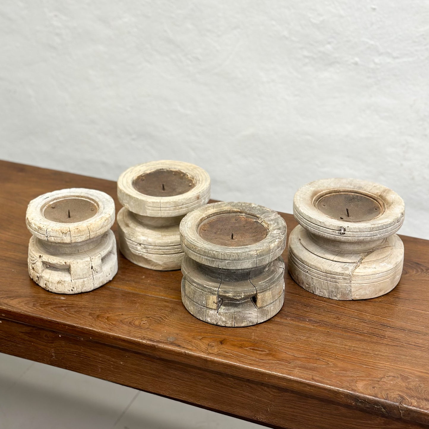 A set of three bleached wooden candle holders in different sizes placed on a wooden surface.