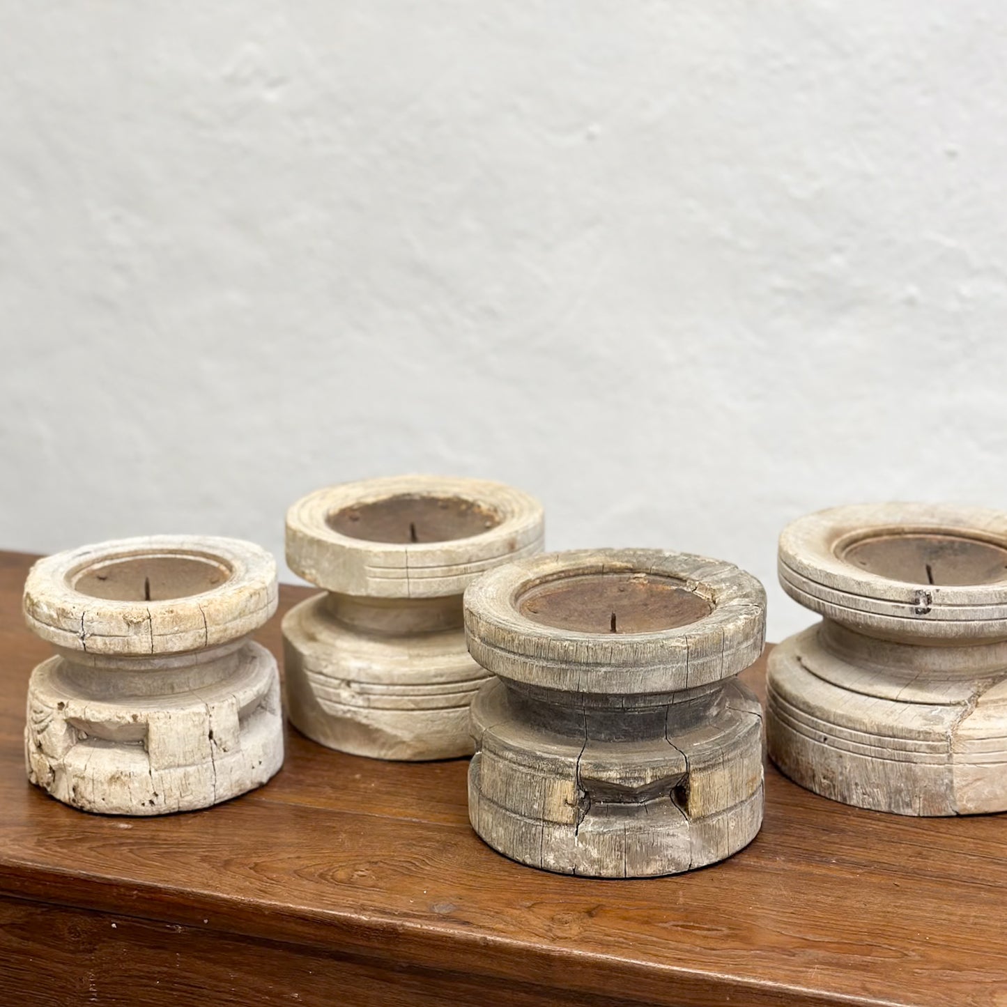 A set of three bleached wooden candle holders in different sizes placed on a wooden surface.