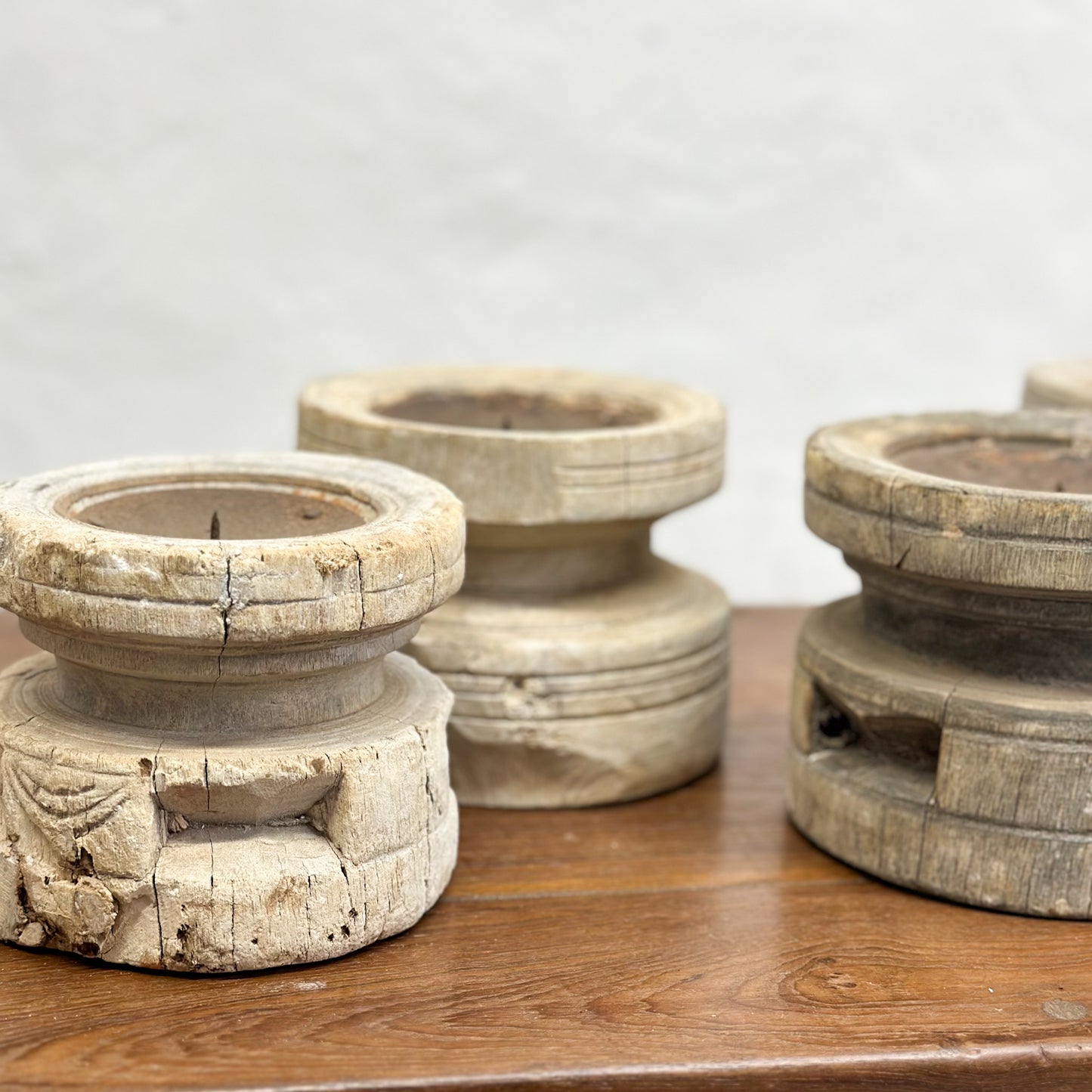 A set of three bleached wooden candle holders in different sizes placed on a wooden surface.
