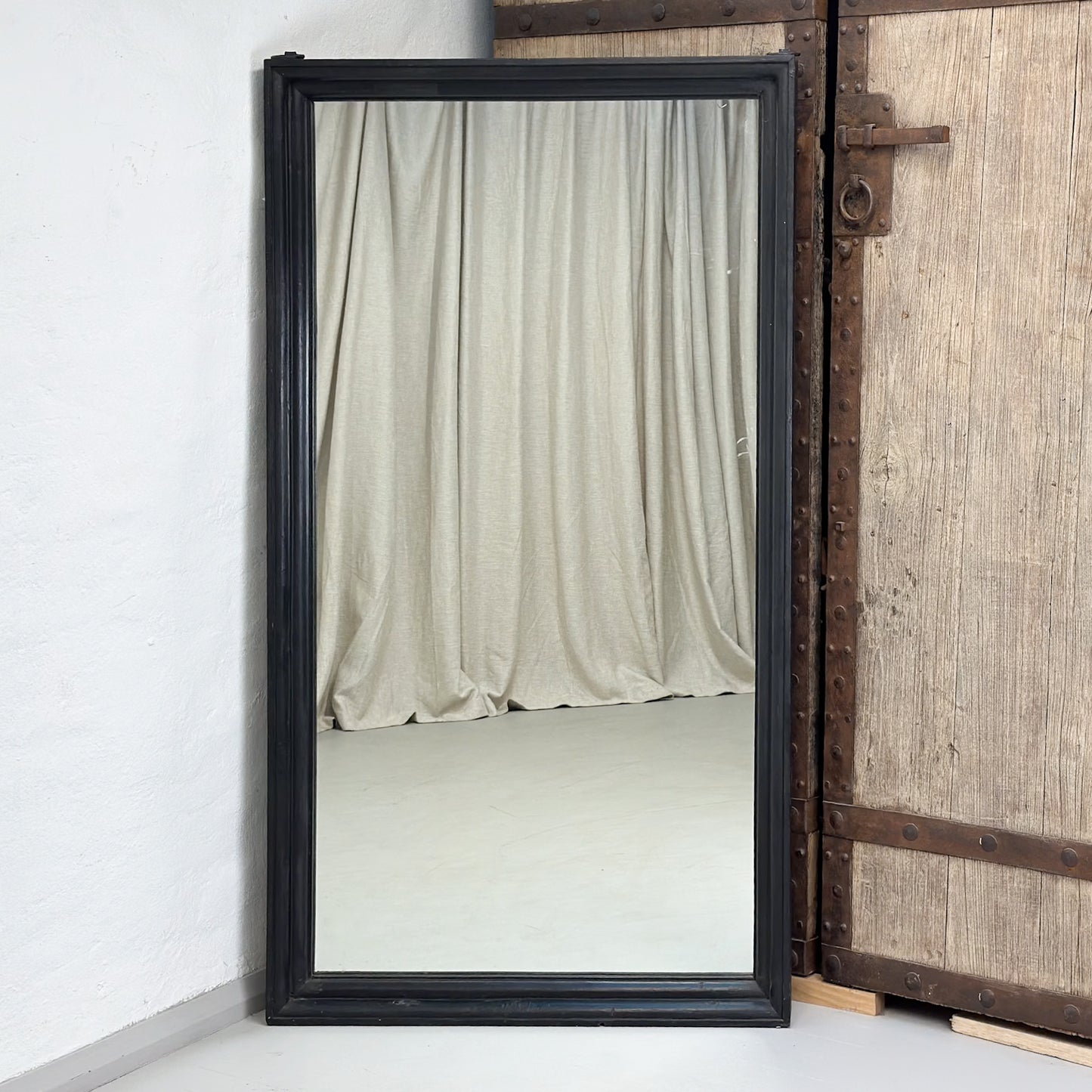 A large rectangular mirror with a teak wooden frame, standing against a wall next to a door.