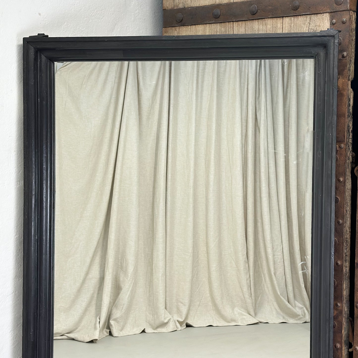 A large rectangular mirror with a teak wooden frame, standing against a wall next to a door.