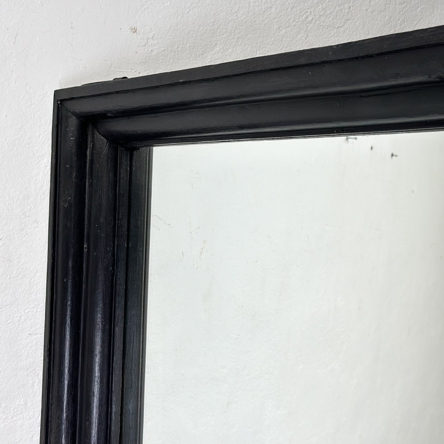 A large rectangular mirror with a teak wooden frame, standing against a wall next to a door.
