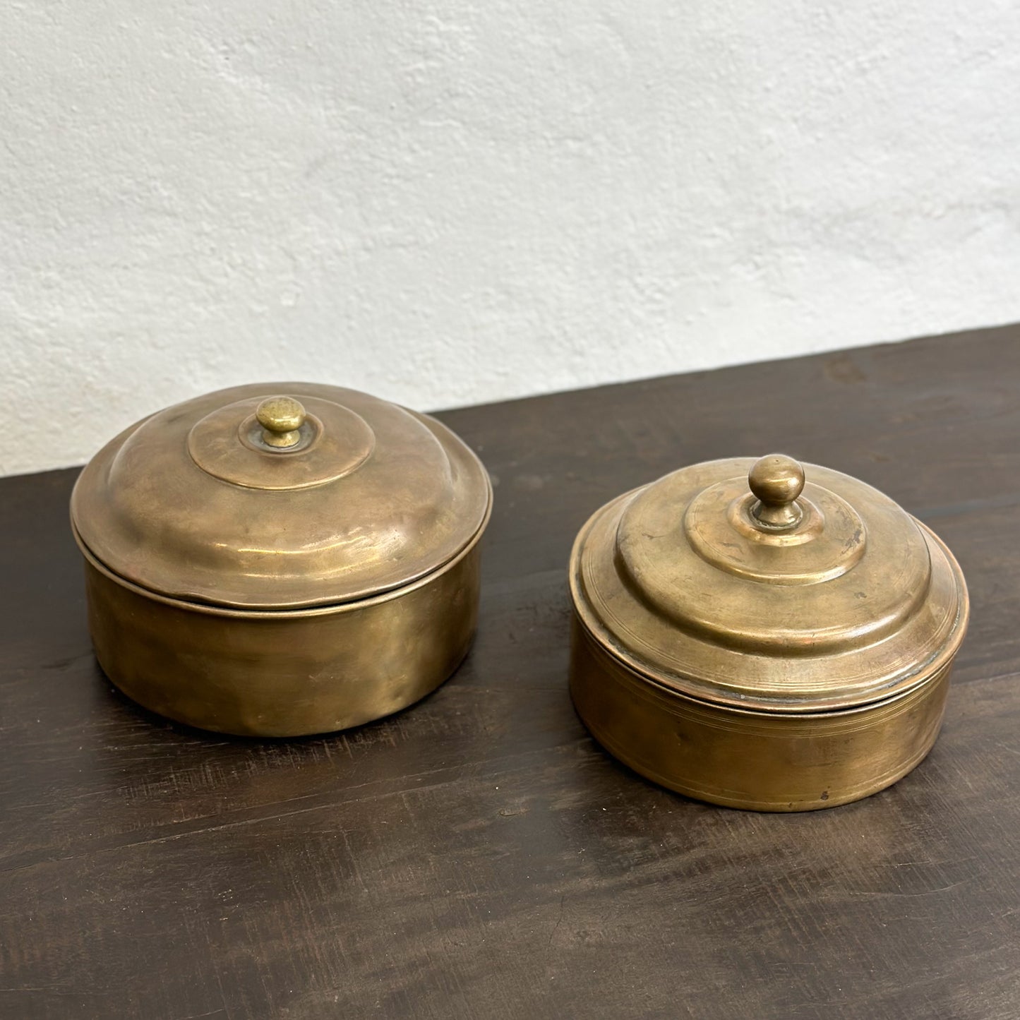 Two brass knob lid chapati boxes with a plain background.