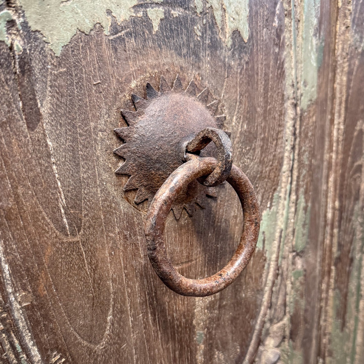 Rustic metal knocker on a wooden door with peeling paint
