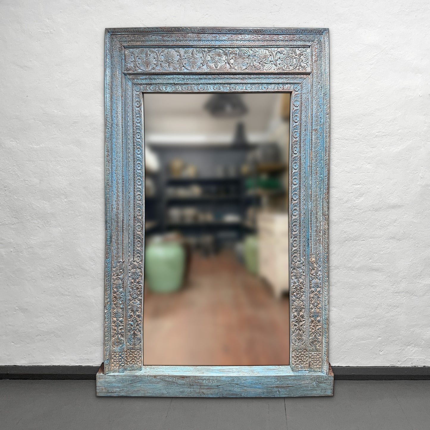 Decorative mirror with ornate blue frame on a plain wall
