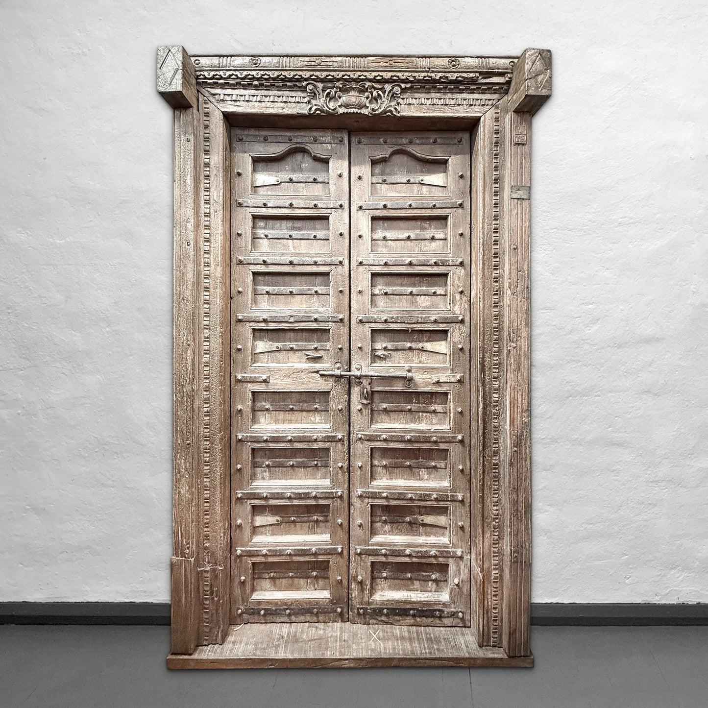Vintage wooden door with intricate carvings on a plain wall.