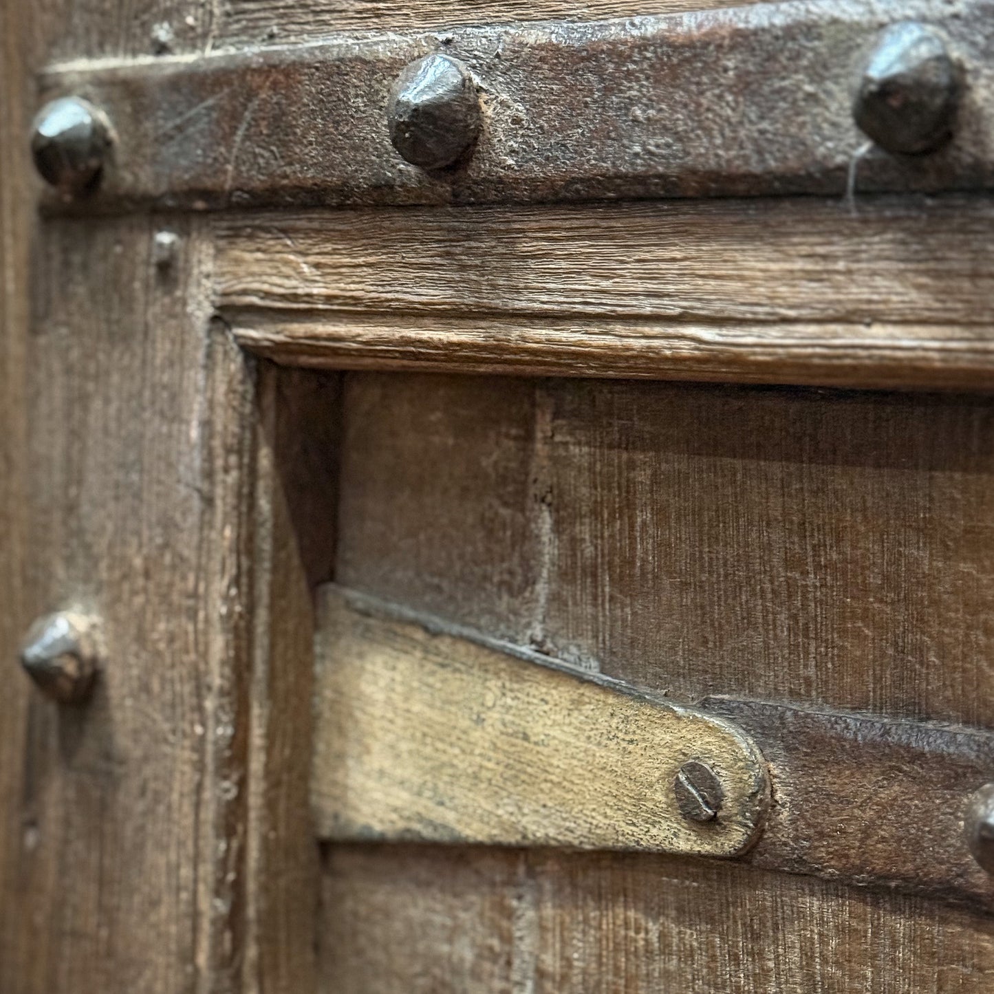Close-up of a wooden door with metal rivets and a hinge.