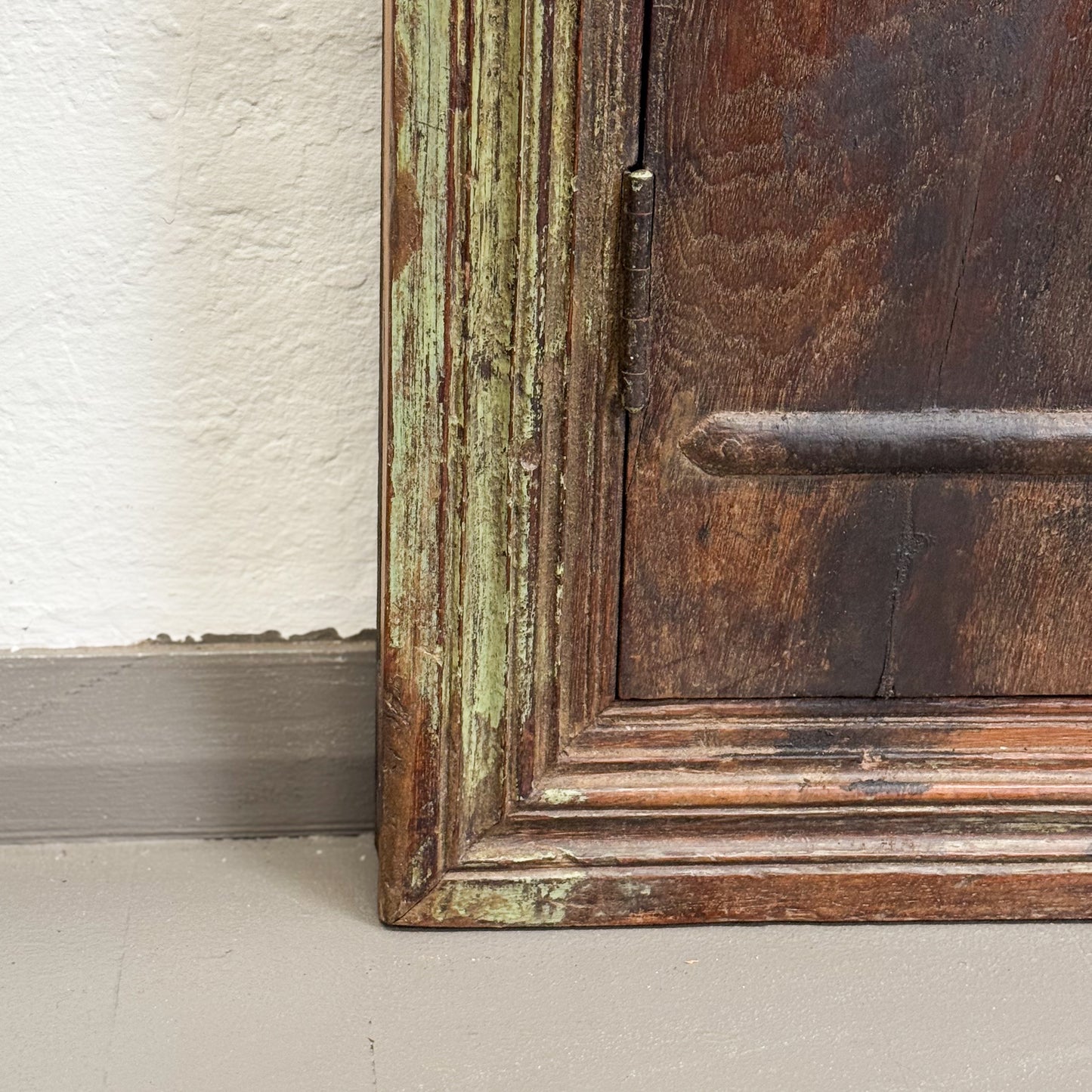 Close-up of a wooden frame with peeling green paint on a white wall.