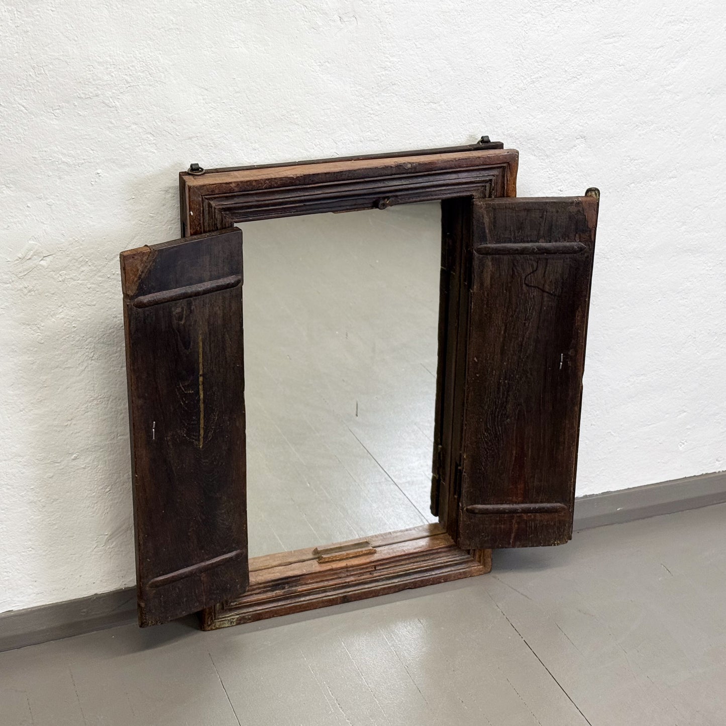 Wooden-framed mirror with a rustic design on a white wall.