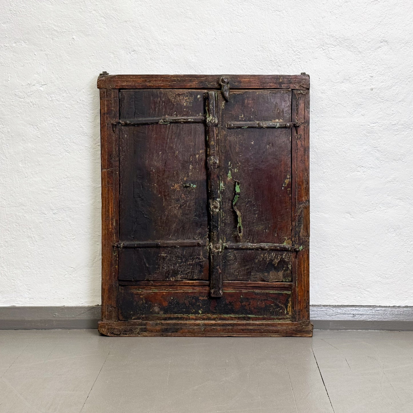 Vintage wooden wardrobe with metal handles against a white brick wall.