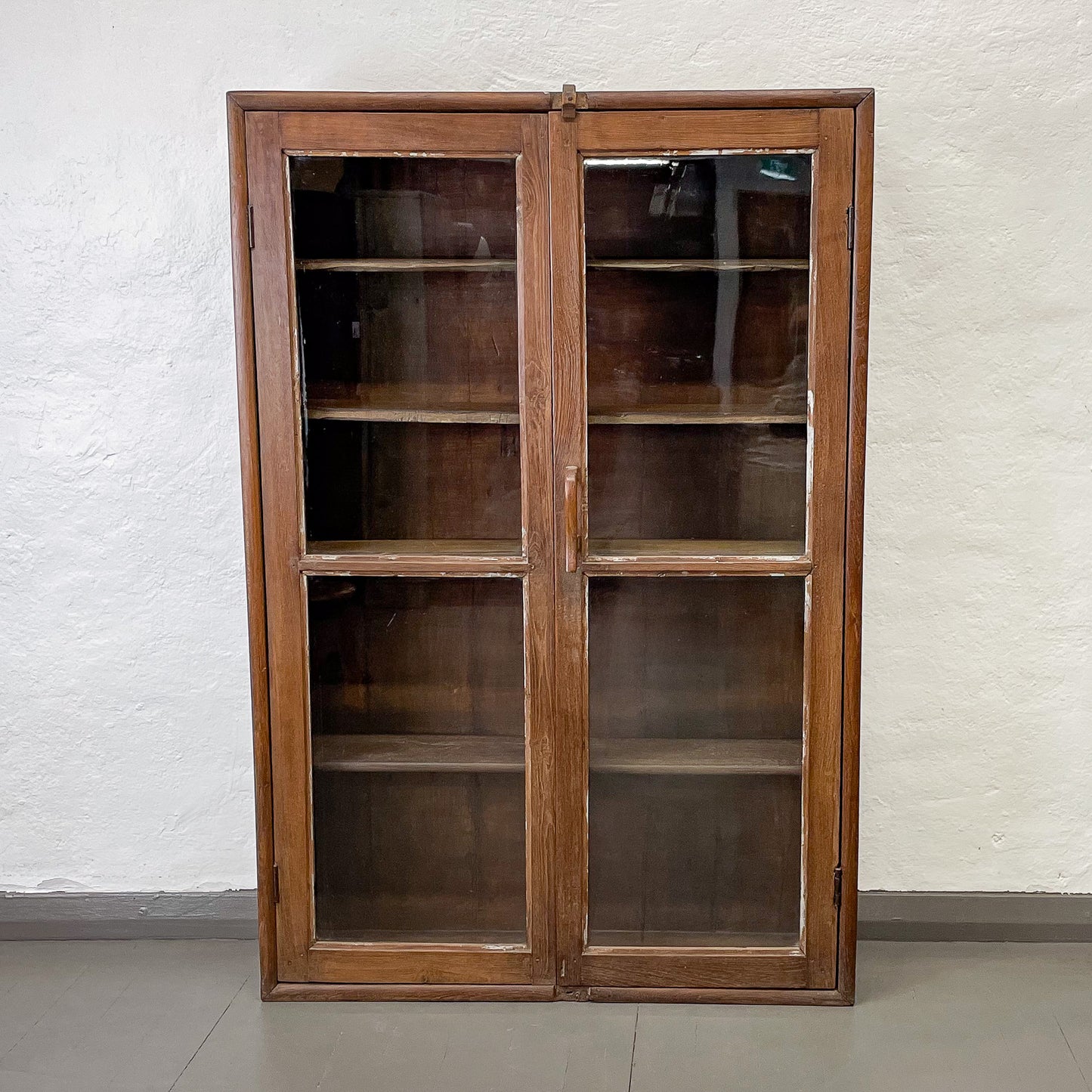 Wooden cabinet with glass doors against a white wall