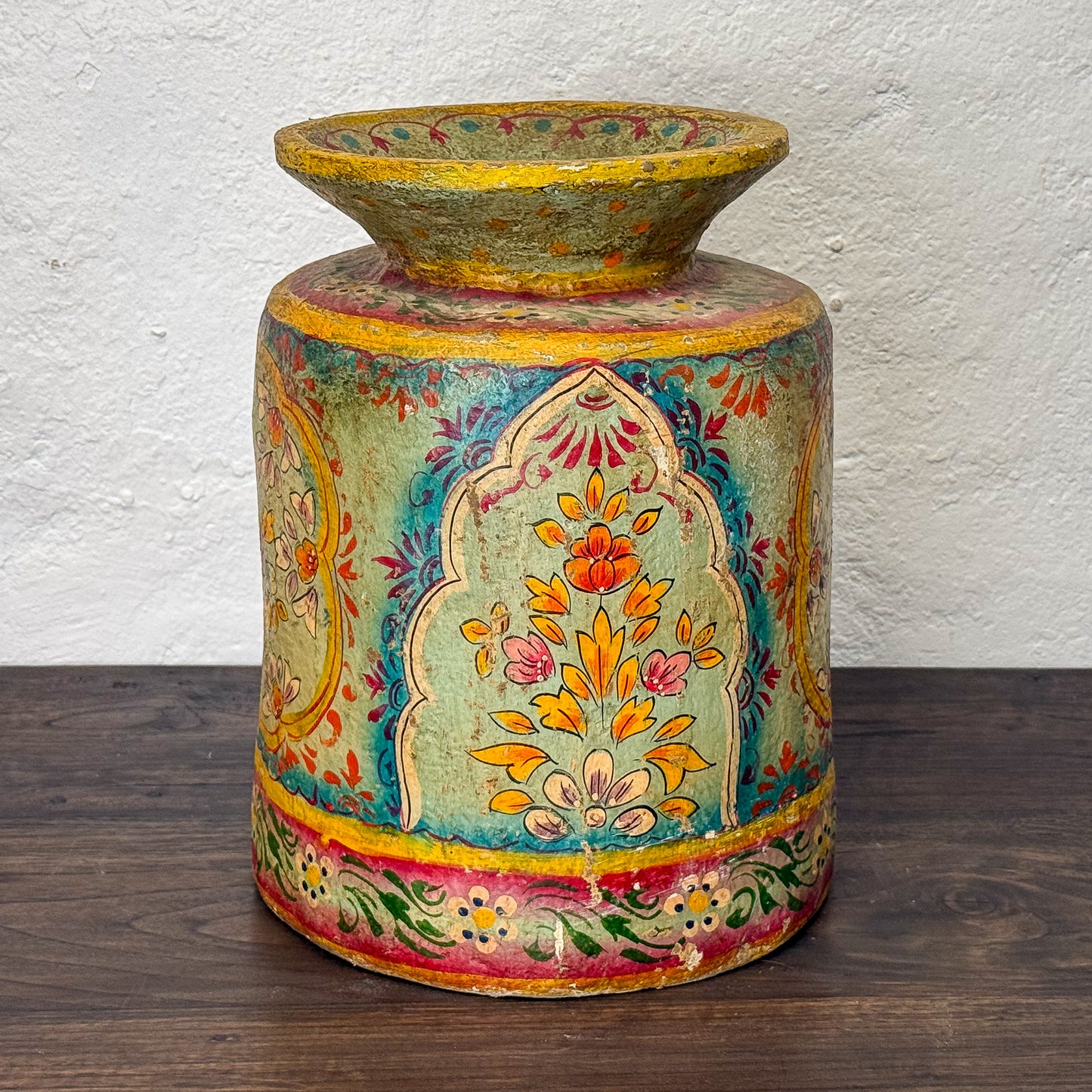 Colorful decorative vase with intricate patterns on a wooden surface and white wall background
