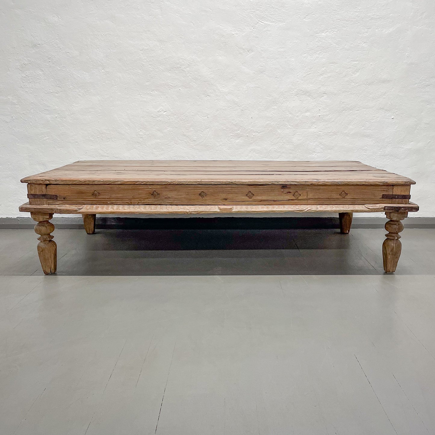 Wooden coffee table with turned legs on a gray floor and white brick wall background