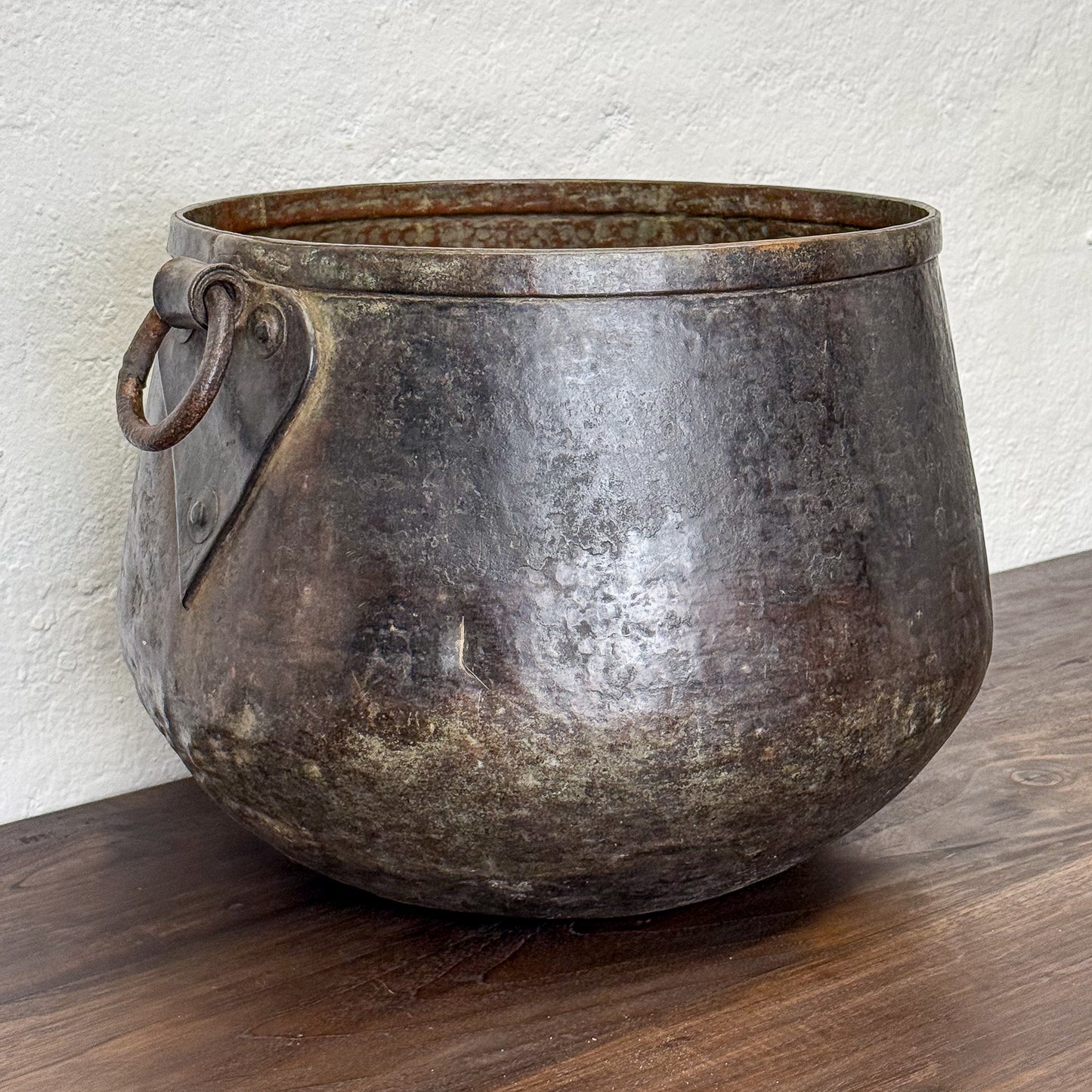 Vintage metal pot with handles on a wooden surface against a white wall