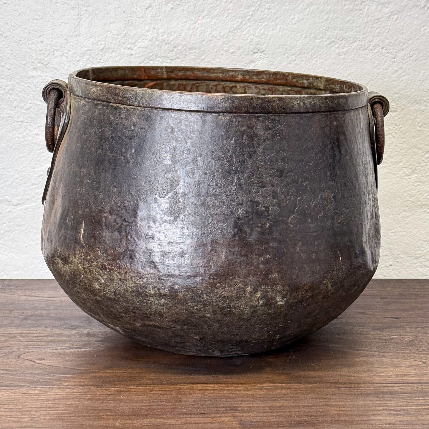 Vintage metal pot with handles on a wooden surface and white wall background