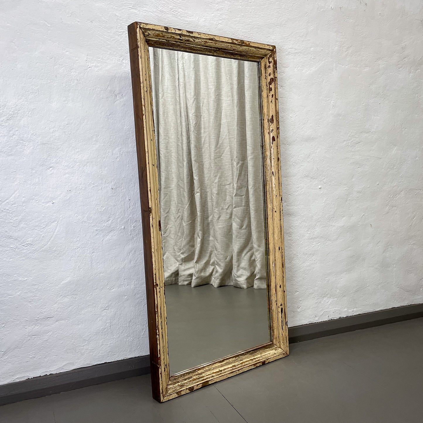 Wooden-framed mirror leaning against a textured white wall.