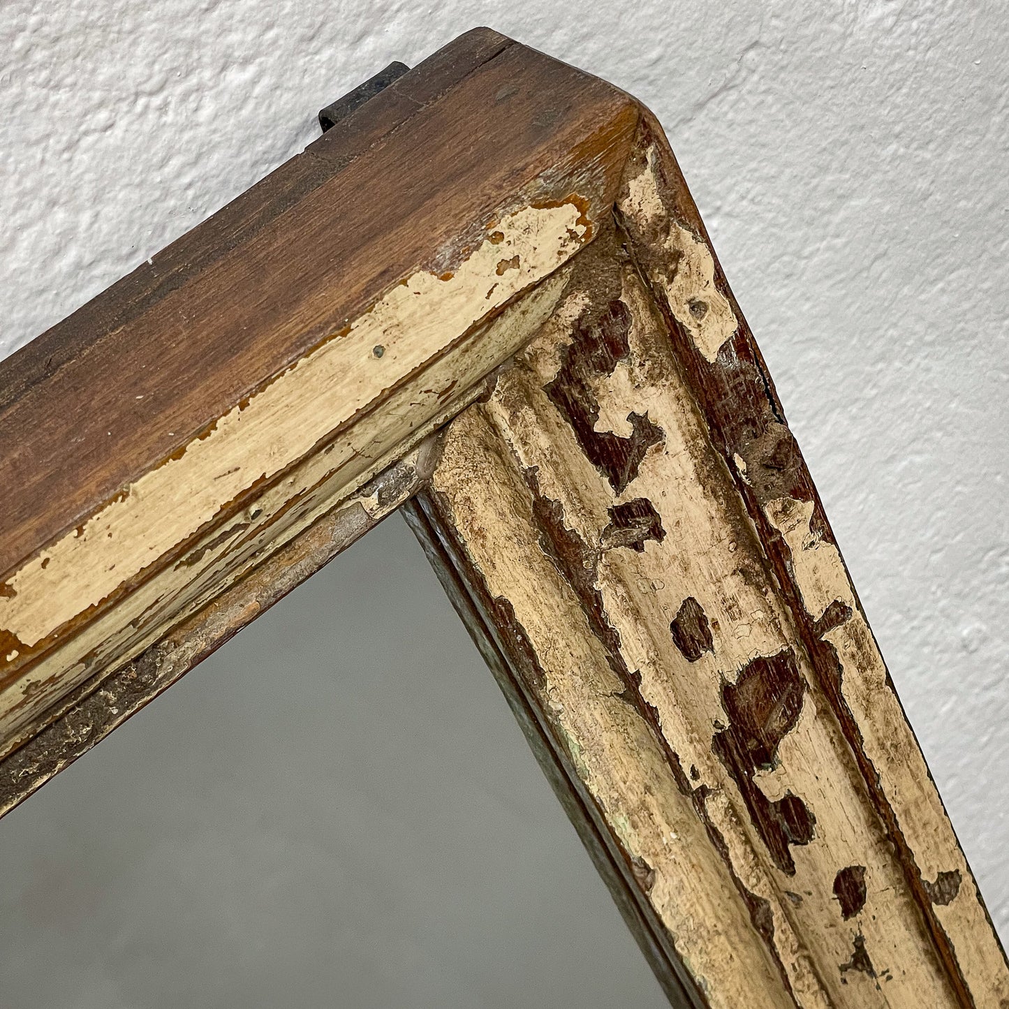 Close-up of a wooden picture frame with peeling paint on a white wall.