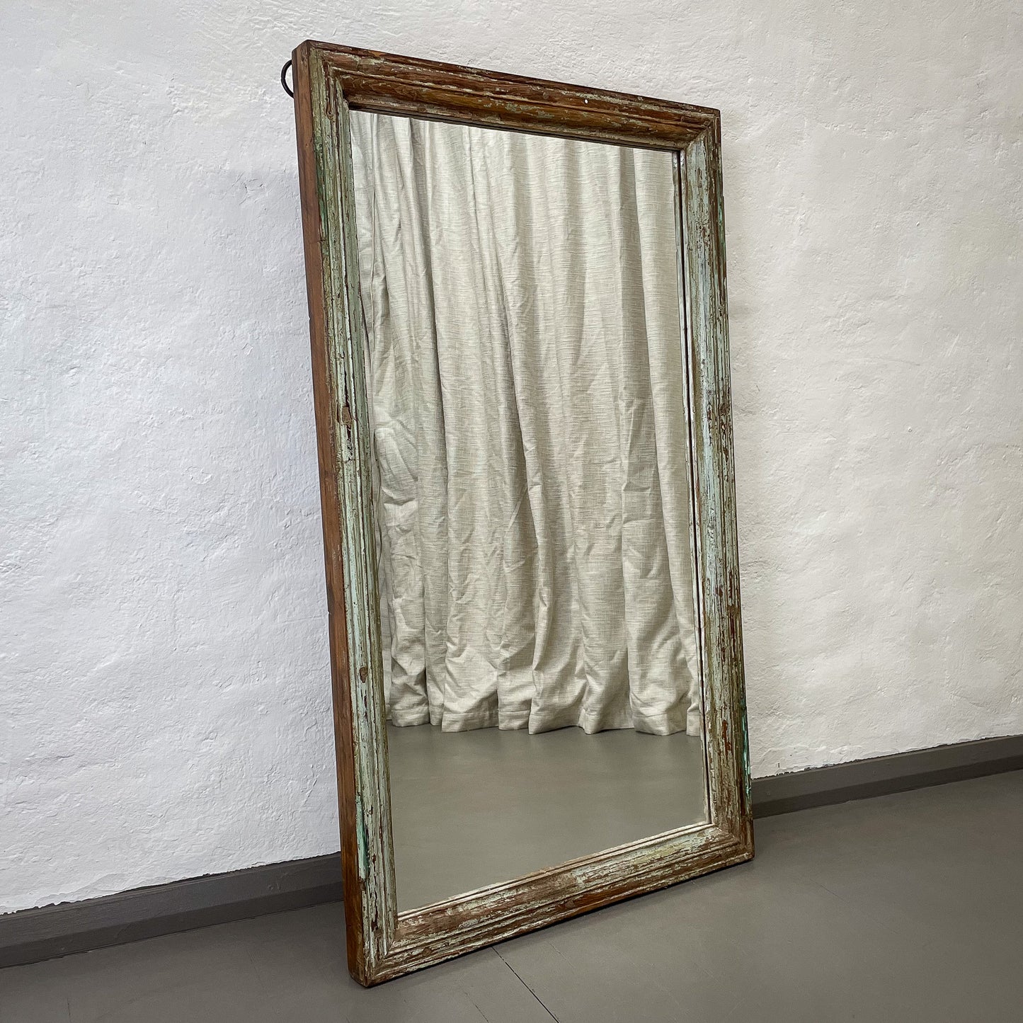 Wooden-framed mirror leaning against a textured white wall.