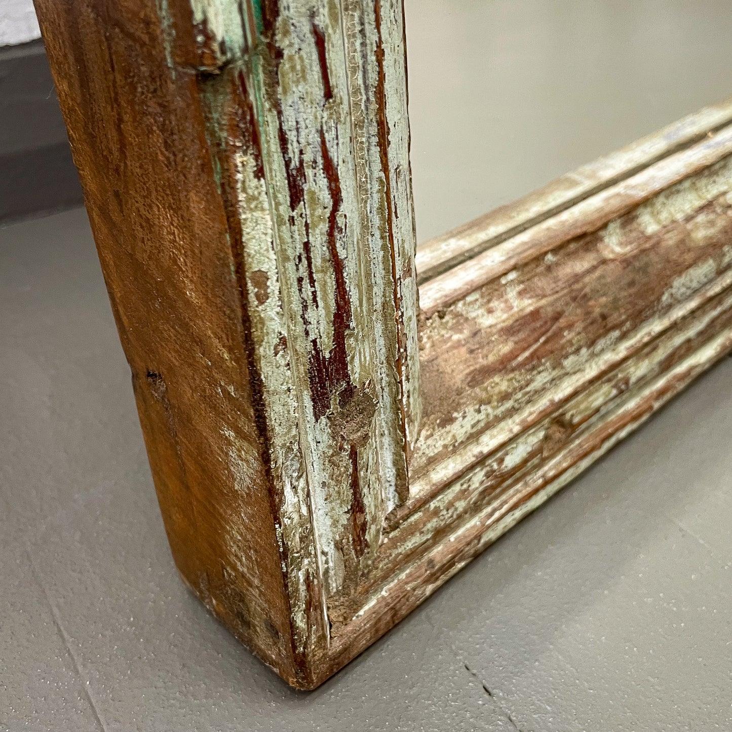 Close-up of a wooden frame with peeling paint on a gray floor.