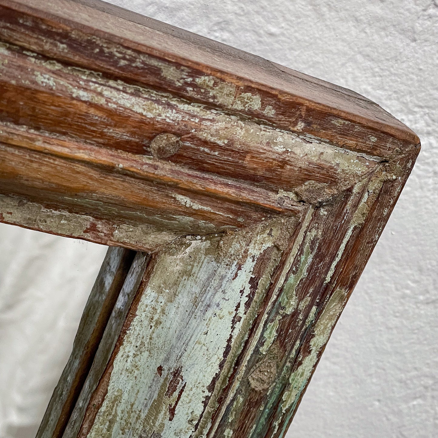 Close-up of a weathered wooden frame with peeling paint on a textured white background