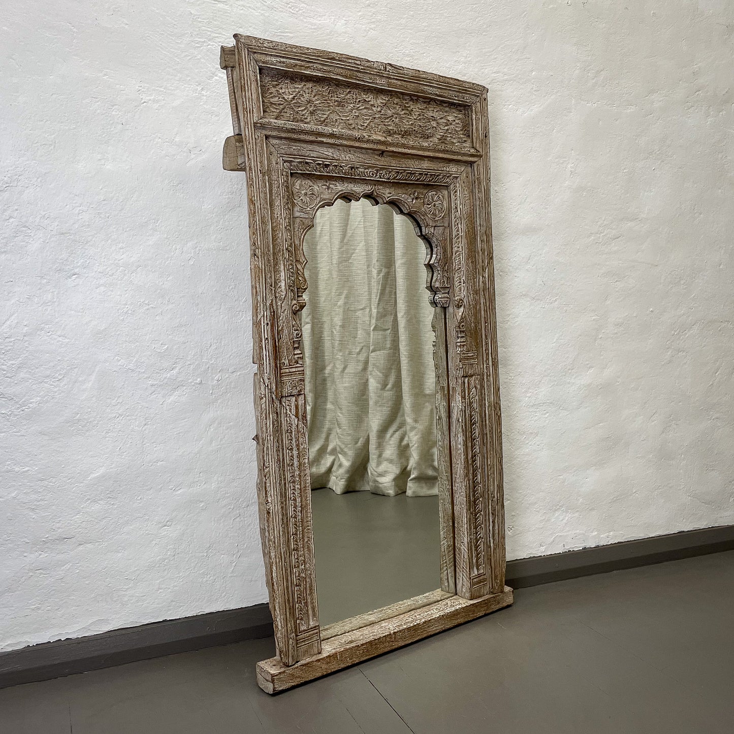 Decorative wooden mirror with intricate carvings on a white wall.