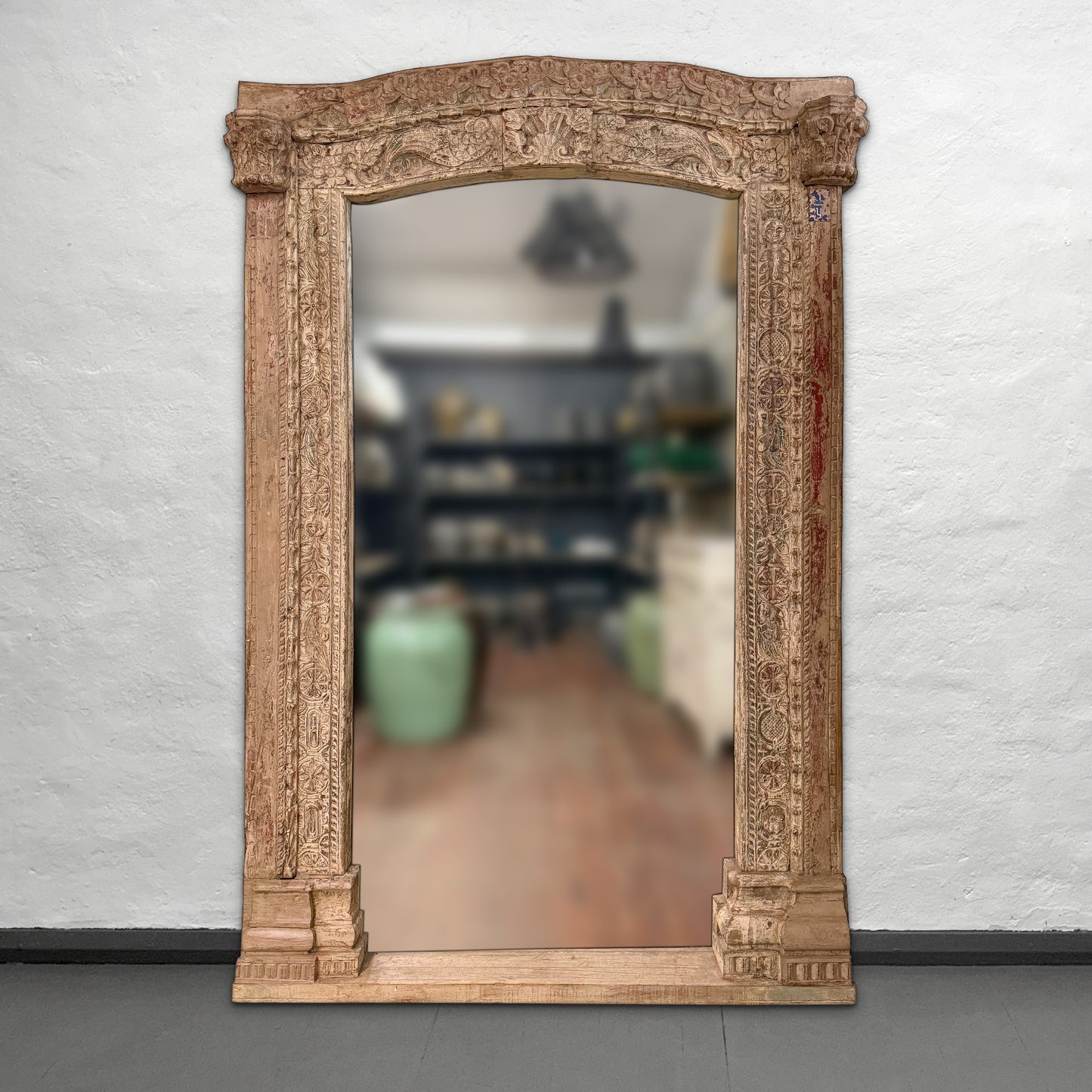 Decorative mirror with an ornate wooden frame on a plain wall.