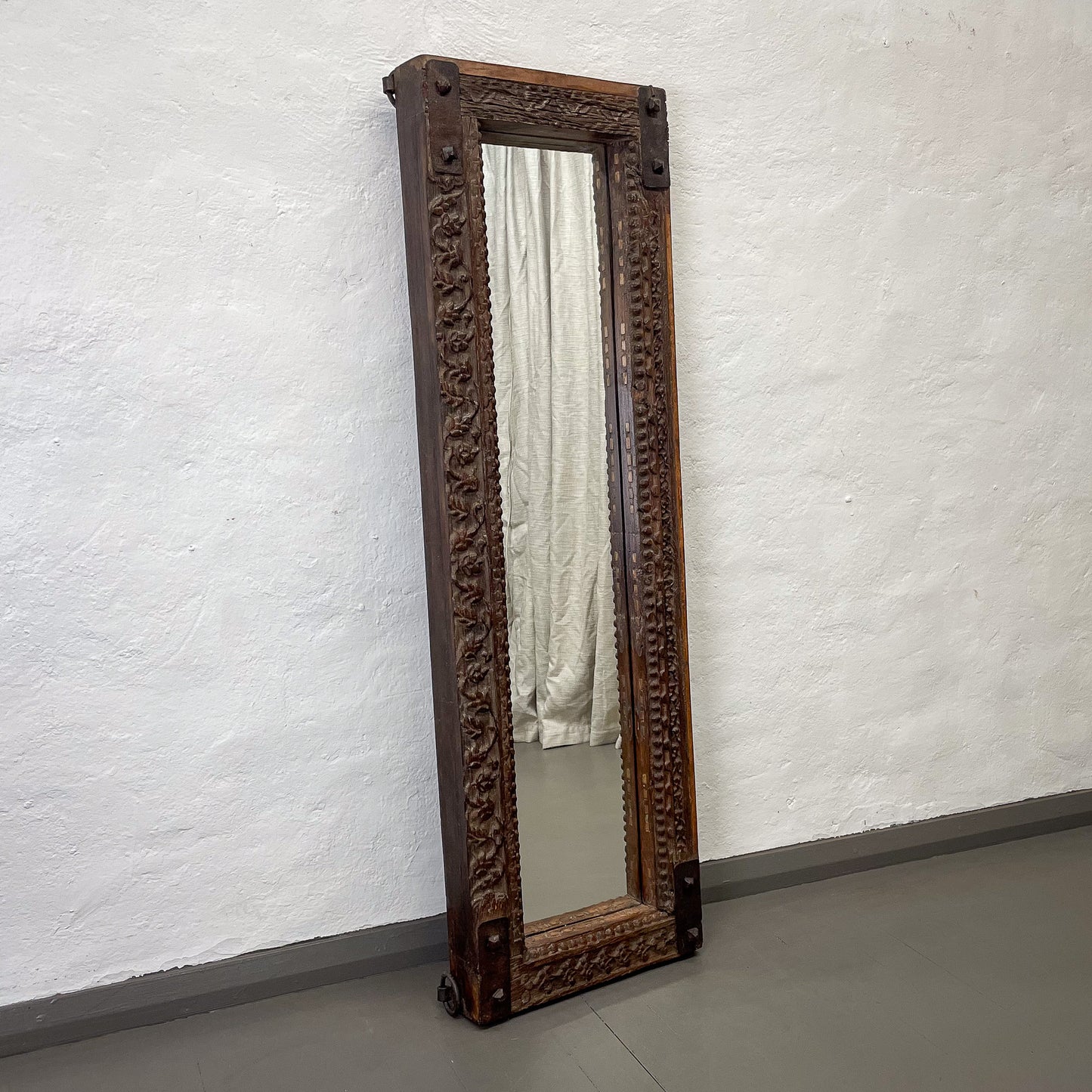 Decorative wooden mirror with intricate carvings on a white wall.