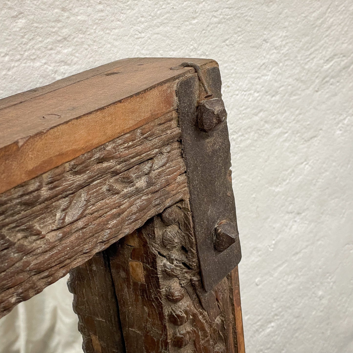 Close-up of a wooden structure with metal brackets against a white wall.