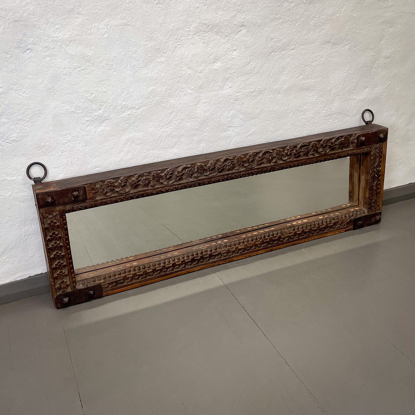 Decorative mirror with intricate carvings on a plain wall.