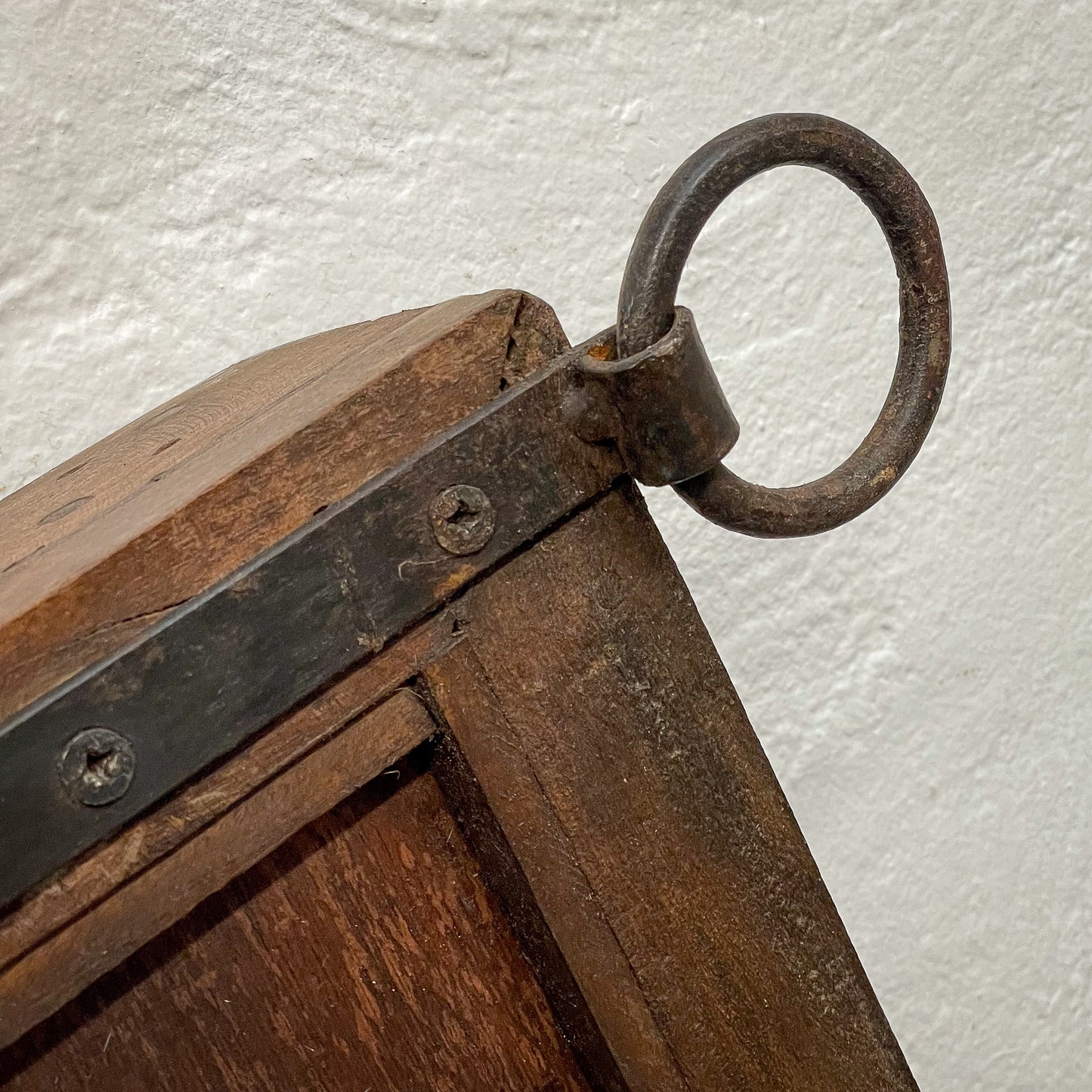 Close-up of a wooden object with metal accents and a ring handle on a white background