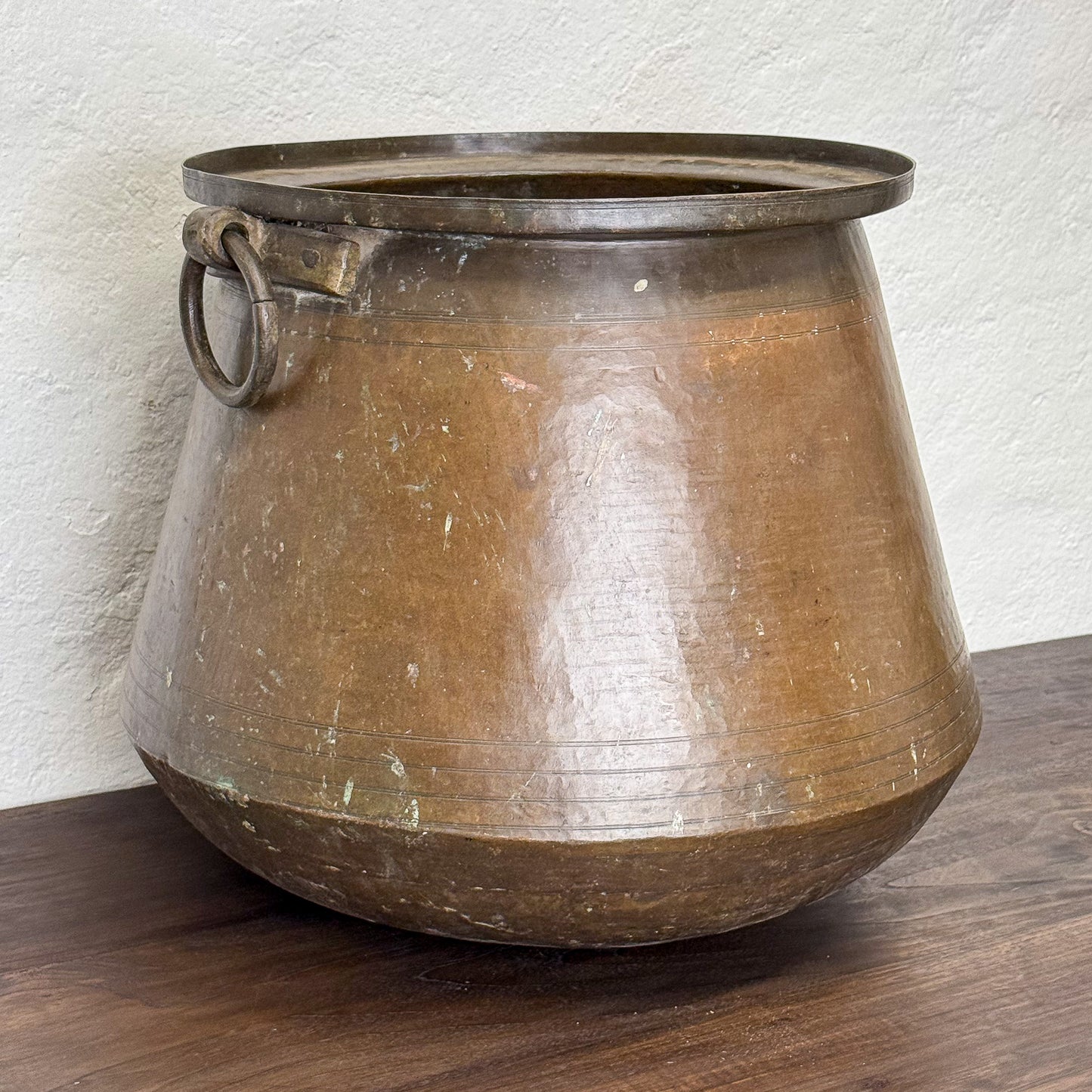 Bronze pot with handles on a wooden surface against a textured white wall
