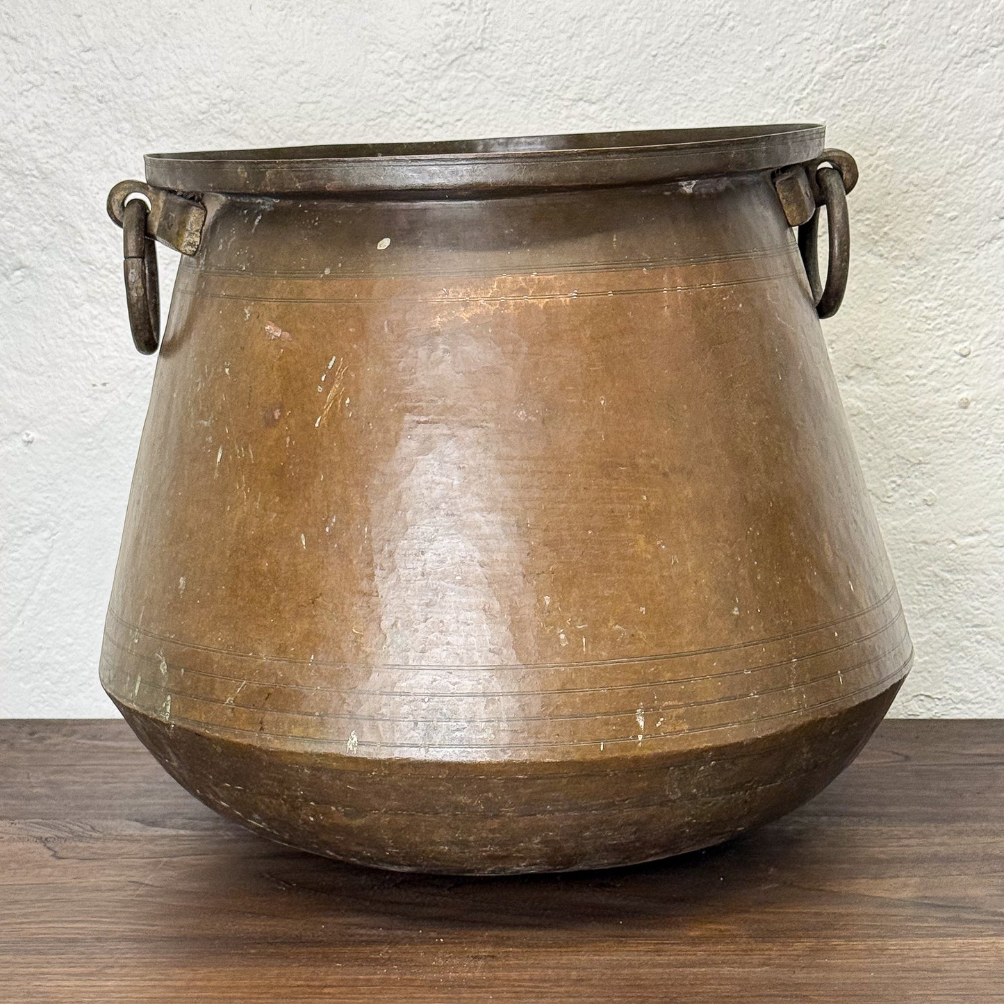 Bronze pot with handles on a wooden surface and white wall background