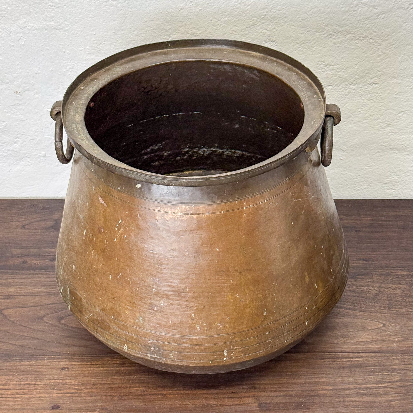 Bronze pot on a wooden surface with a white wall background