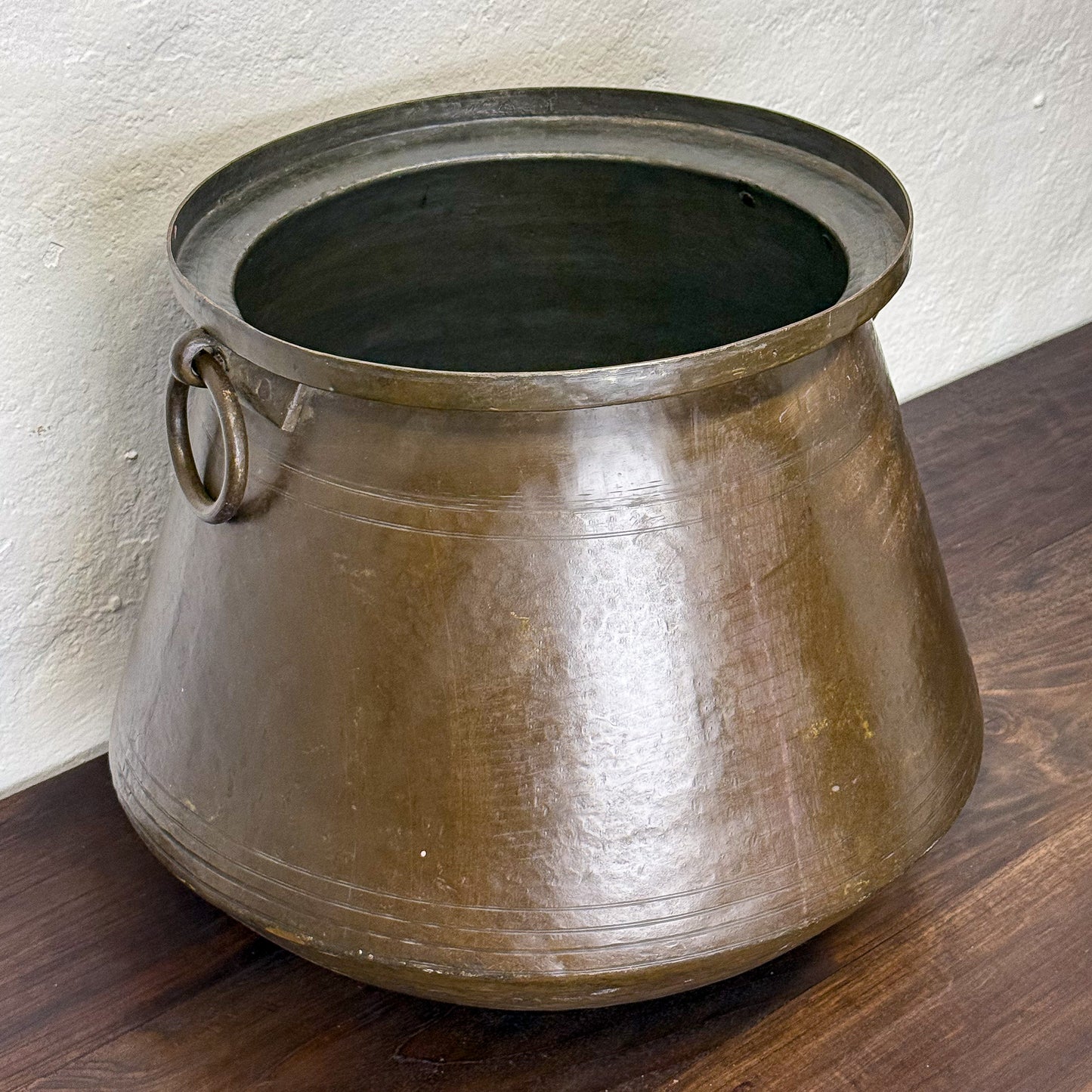 Bronze pot with handles on a wooden surface against a white wall