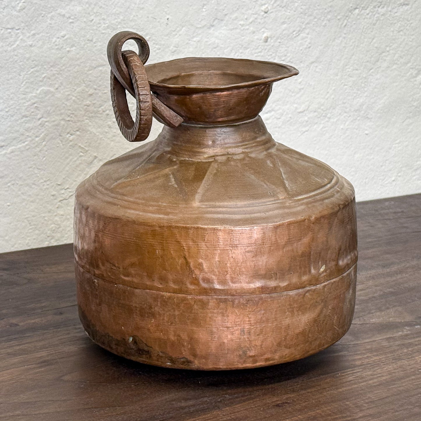 Vintage copper water jug on a wooden surface with a white wall background
