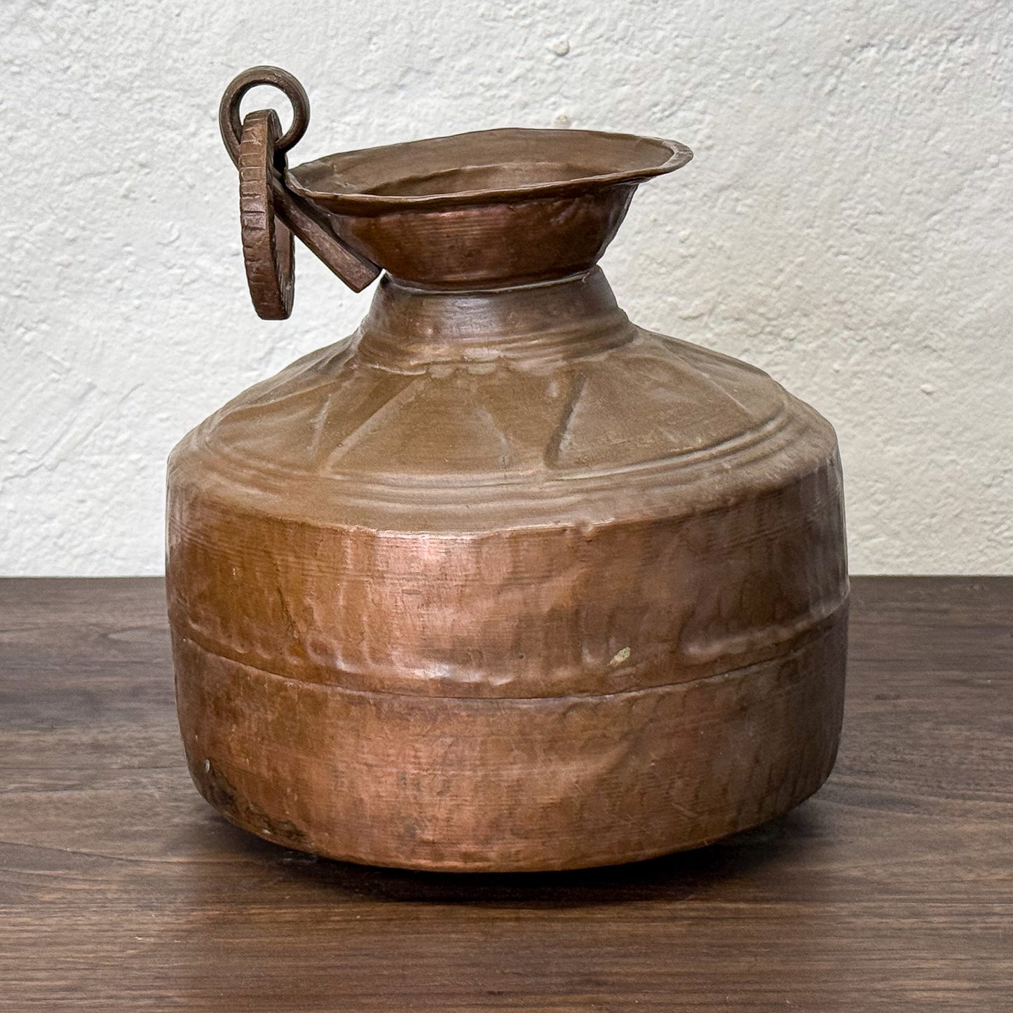Vintage copper water jug on a wooden surface with a white textured wall background