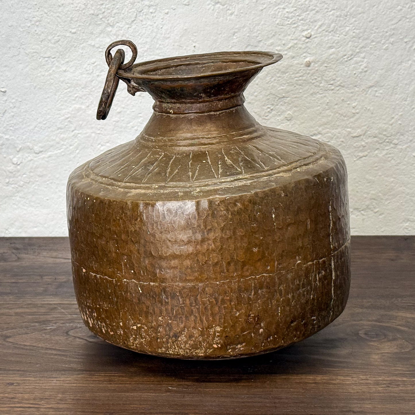 Brown ceramic jar with lid on a wooden surface against a white wall
