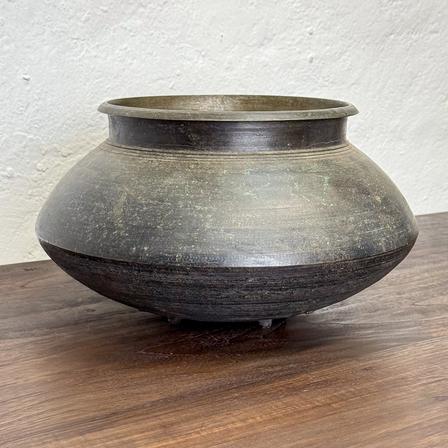 Vintage-style pot on a wooden surface with a white textured wall background