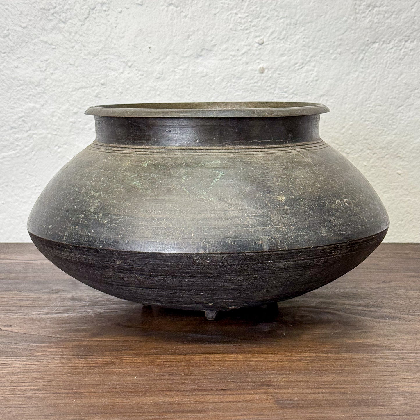 Large ceramic pot on a wooden surface with a textured white wall background