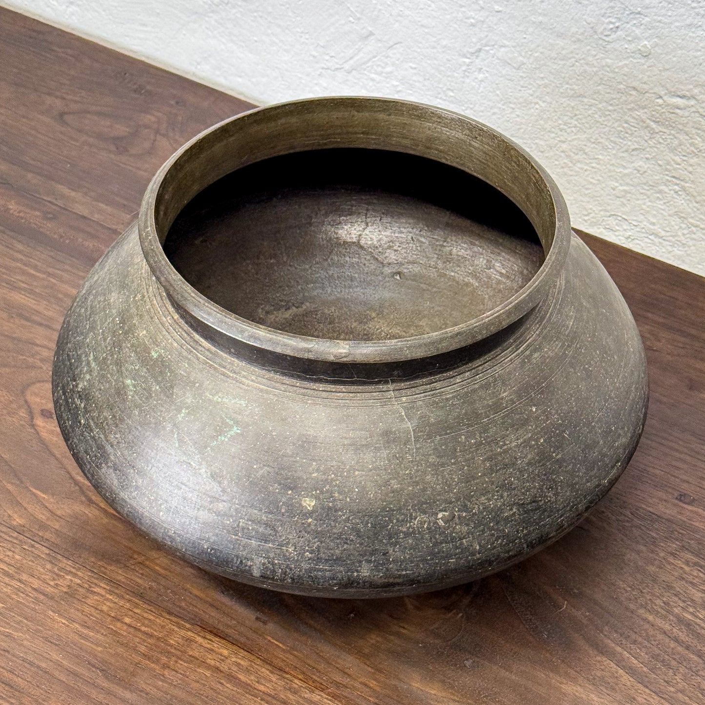 Bronze pot on a wooden surface with a white wall background