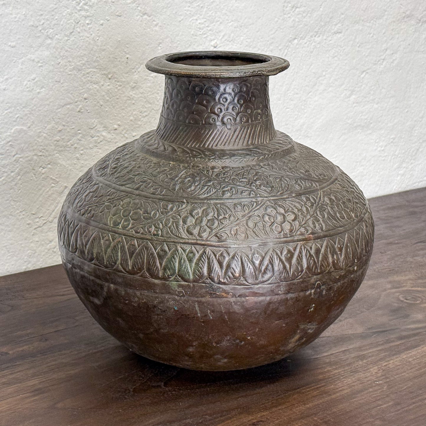 Decorative bronze vase with intricate patterns on a wooden surface.