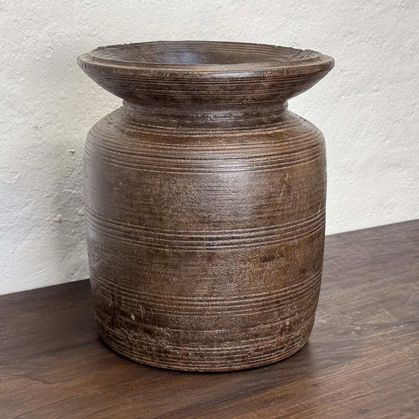 Brown ceramic vase on a wooden surface with a white textured wall background