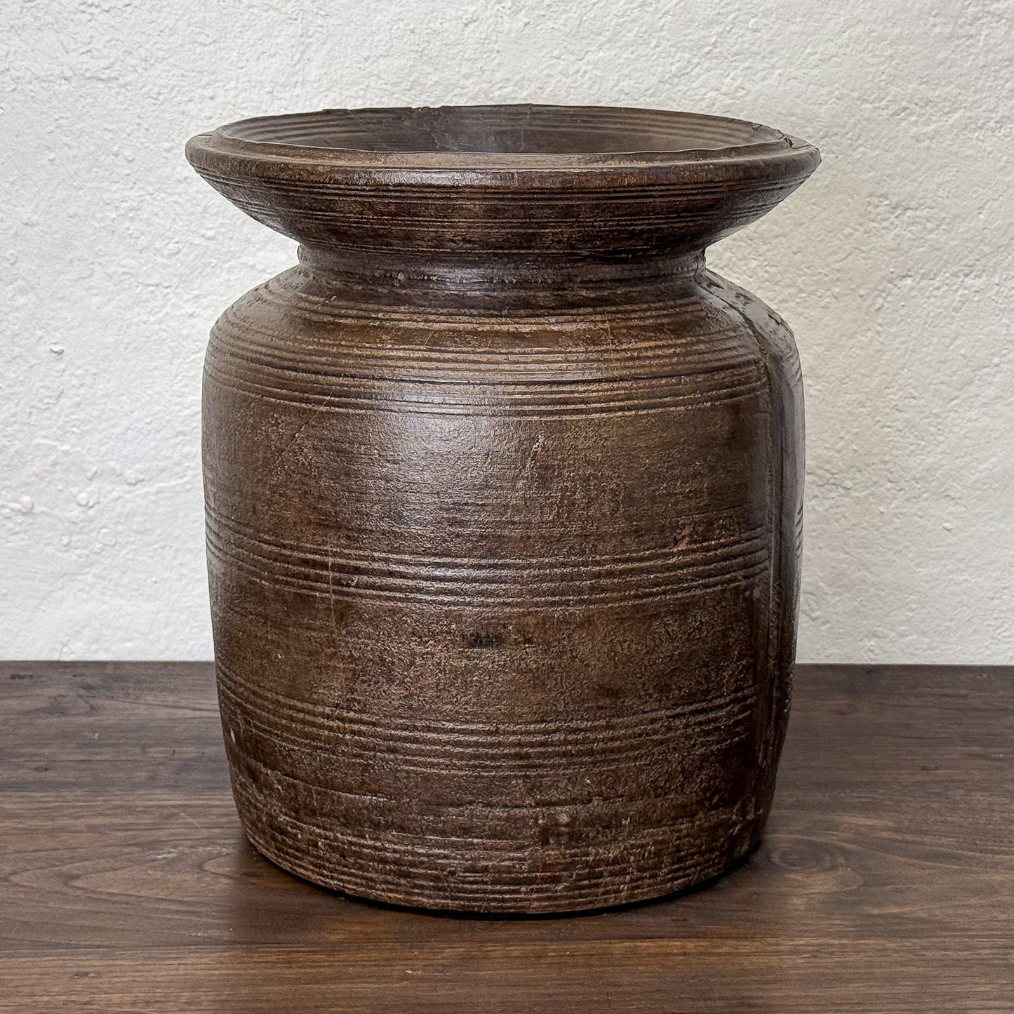 Brown textured vase on a wooden surface with a white wall background