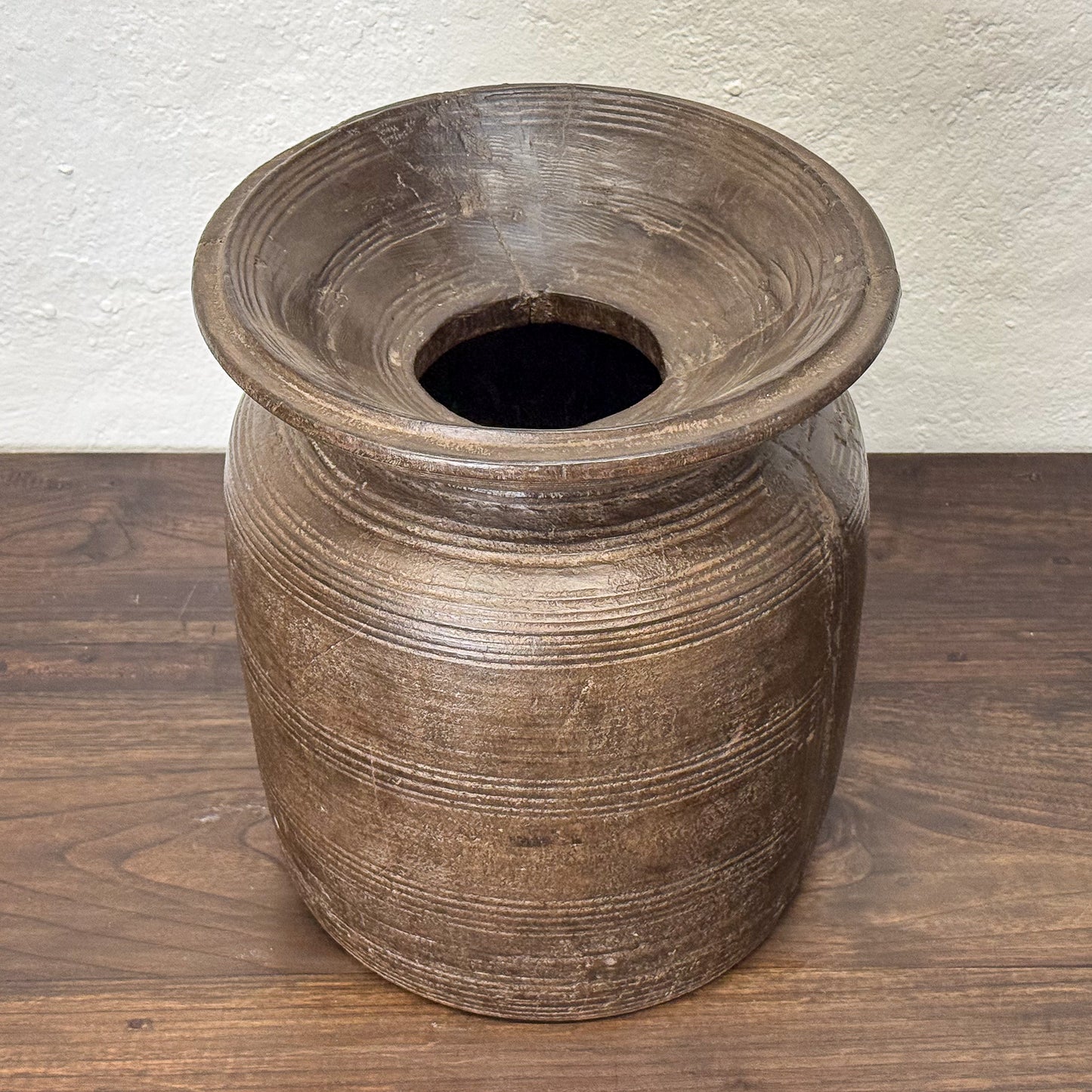Brown ceramic vase on a wooden surface with a white textured wall background