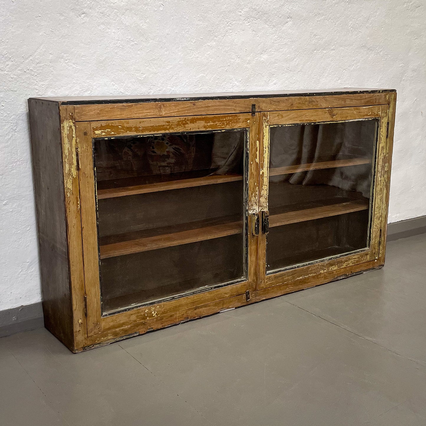 Vintage wooden cabinet with glass doors on a plain floor.